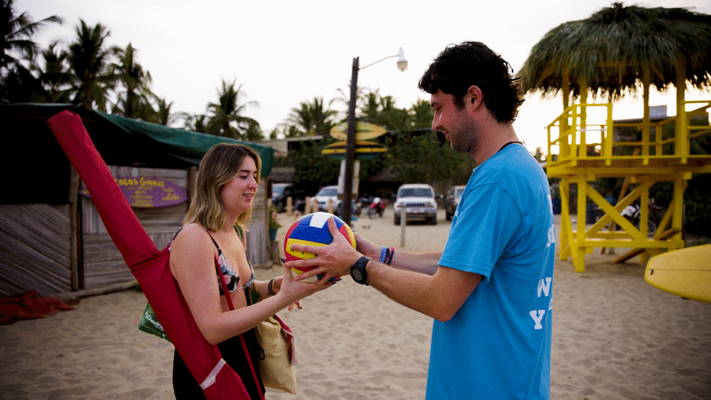 Mack Linstead, Beach Sherpa Founder, handing a multi-color volleyball to Karin, a beachgoer who needed help carrying her things.